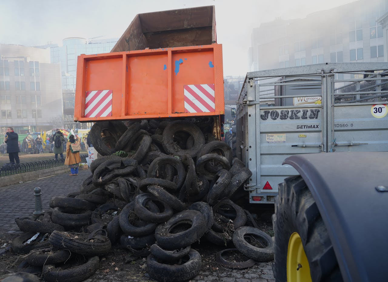 Protest in city street featuring dump truck unloading tires, surrounded by people and buildings.