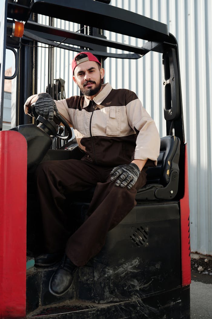 Male forklift operator in industrial uniform sitting on a forklift outdoors.